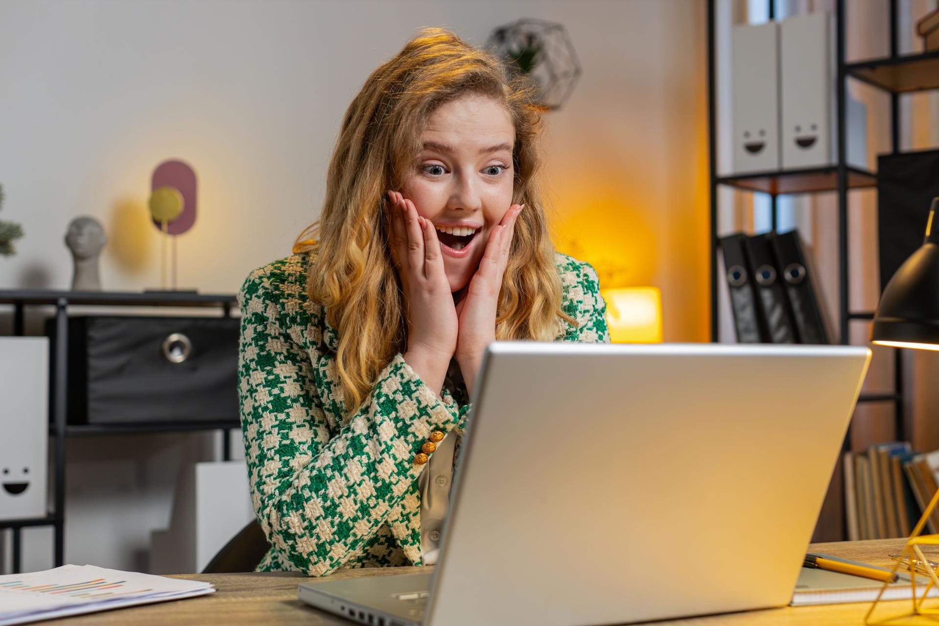 Happy amazed businesswoman working on laptop shocked by sudden victory game winning wow good news